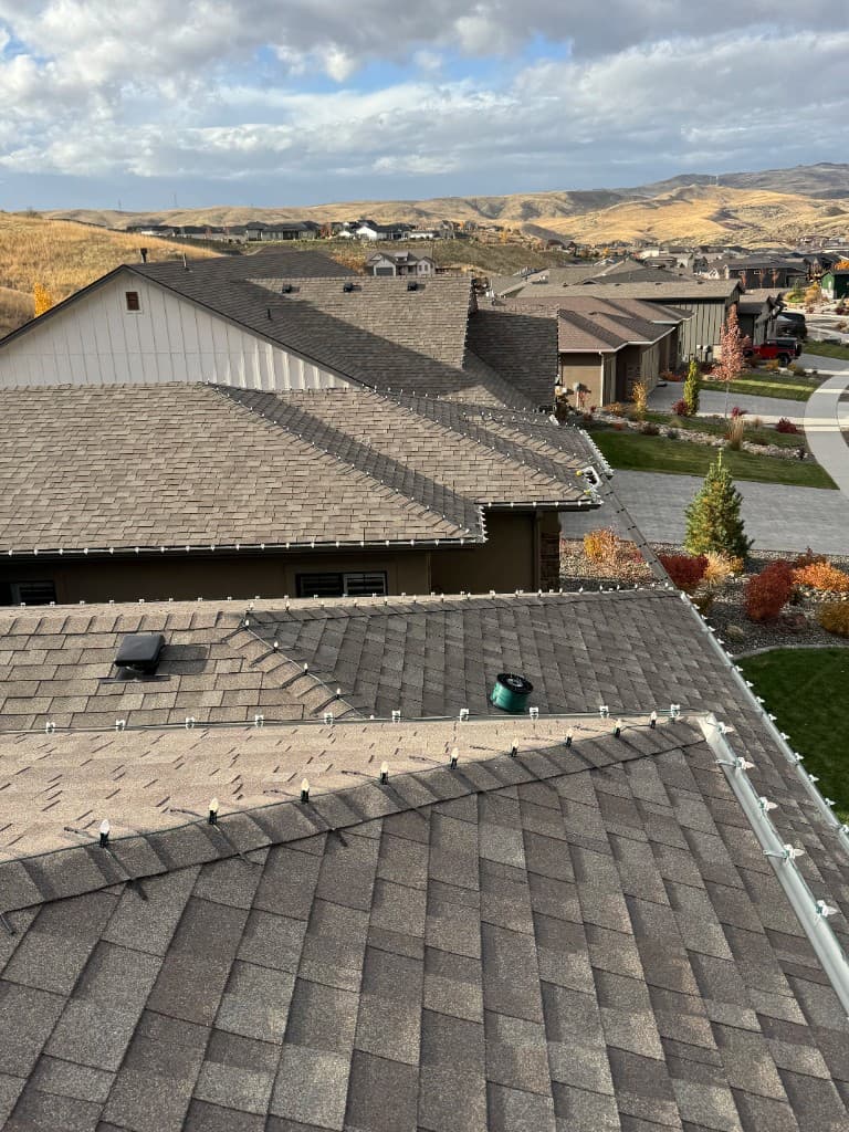 Installer working on Christmas lights from ladder on Boise home exterior