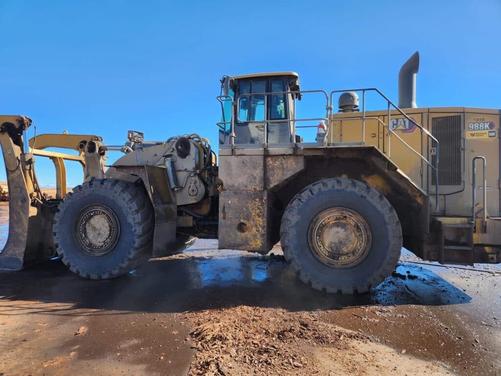 CAT 988K wheel loader covered in mud on a wet yard — heavy equipment demucking